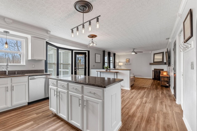 kitchen with white cabinets, dishwasher, open floor plan, hanging light fixtures, and a sink