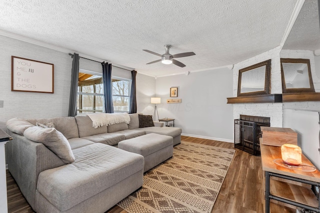 living area with baseboards, dark wood-style floors, ceiling fan, ornamental molding, and a fireplace