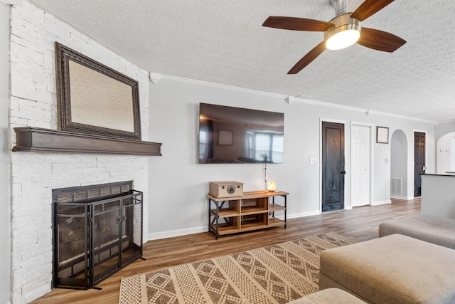 living area featuring arched walkways, crown molding, visible vents, a stone fireplace, and wood finished floors