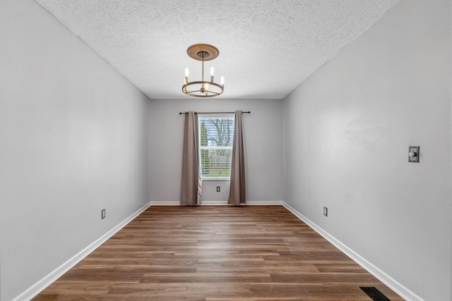 empty room featuring baseboards, visible vents, dark wood-type flooring, a textured ceiling, and a chandelier