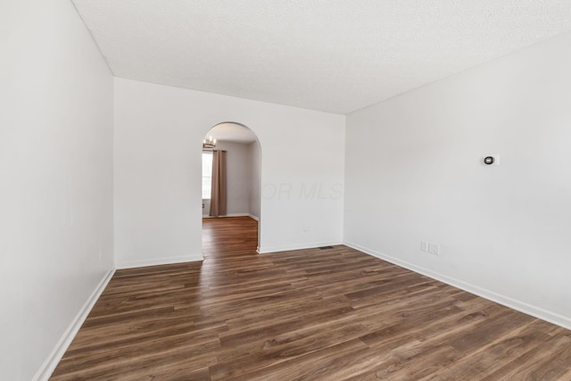 spare room featuring arched walkways, a textured ceiling, dark wood-style floors, and baseboards