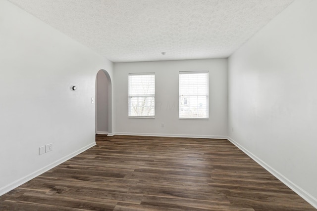 empty room featuring arched walkways, dark wood finished floors, a textured ceiling, and baseboards