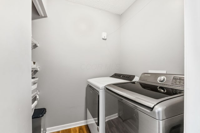 laundry area featuring a textured ceiling, washing machine and dryer, laundry area, wood finished floors, and baseboards