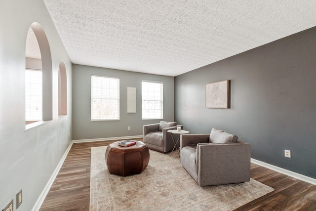 living area featuring arched walkways, a textured ceiling, baseboards, and wood finished floors