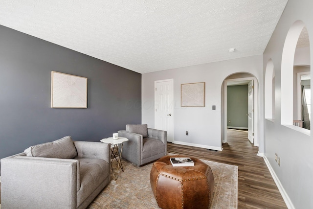 living room with dark wood-type flooring, a textured ceiling, and baseboards