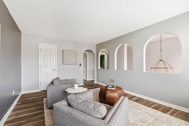 living area featuring arched walkways, dark wood finished floors, a textured ceiling, and baseboards