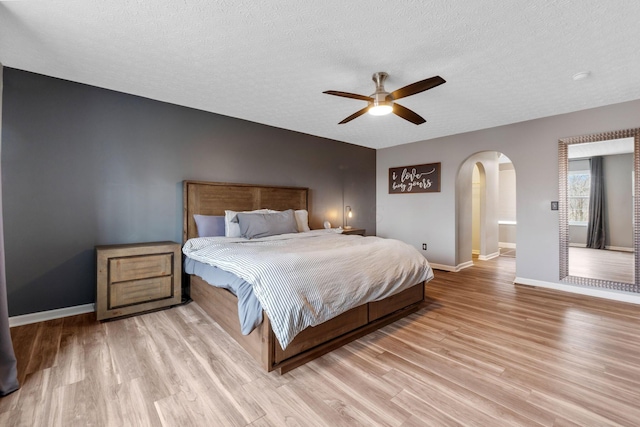 bedroom featuring arched walkways, baseboards, a textured ceiling, and light wood finished floors