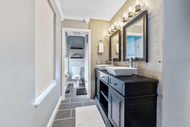 full bathroom featuring a textured ceiling, double vanity, a sink, and toilet