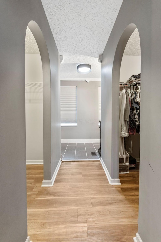 hallway featuring baseboards, a textured ceiling, arched walkways, and wood finished floors