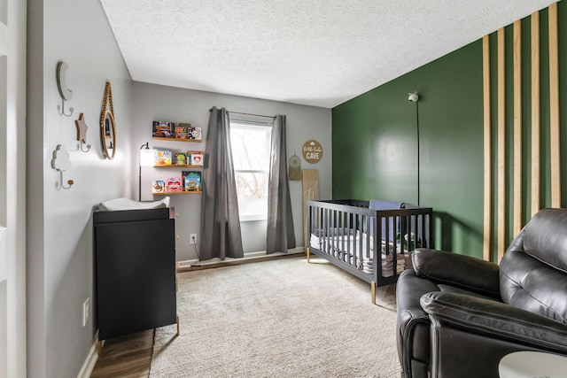 carpeted bedroom featuring a textured ceiling, a crib, and baseboards