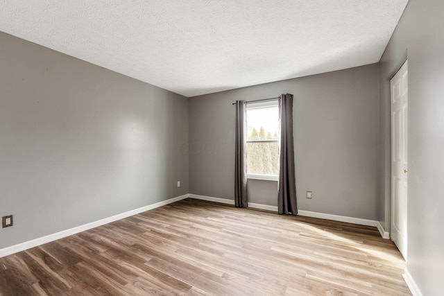 unfurnished room featuring light wood-type flooring, baseboards, and a textured ceiling