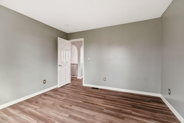 empty room featuring arched walkways, wood finished floors, visible vents, and baseboards