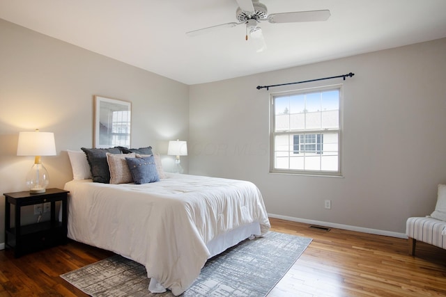 bedroom with a ceiling fan, wood finished floors, visible vents, and baseboards