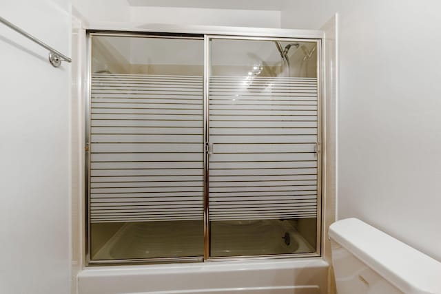 bathroom featuring toilet and shower / bath combination with glass door