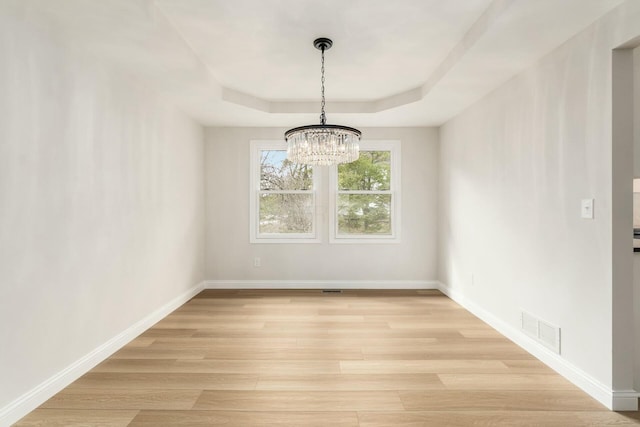 unfurnished dining area with baseboards, a tray ceiling, visible vents, and light wood-style floors