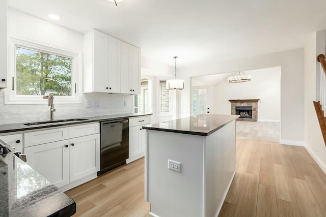 kitchen featuring black dishwasher, a fireplace, tasteful backsplash, a sink, and light wood-type flooring