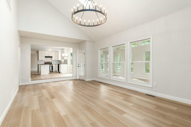 unfurnished living room featuring visible vents, baseboards, light wood-style flooring, an inviting chandelier, and high vaulted ceiling