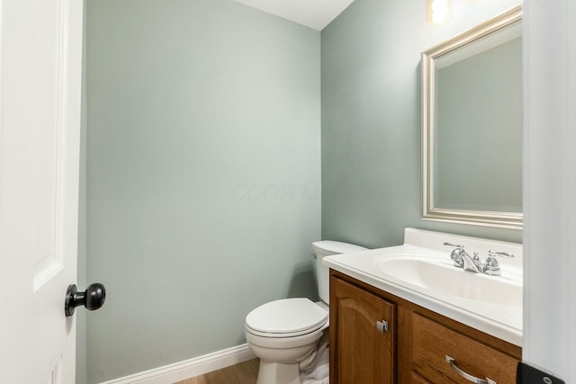 half bathroom with baseboards, vanity, and toilet