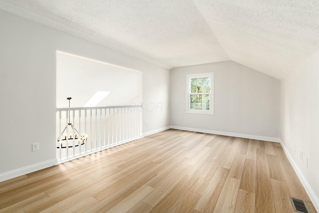 additional living space featuring light wood-style floors, visible vents, lofted ceiling with skylight, and a textured ceiling