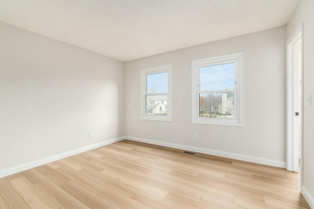 unfurnished room featuring light wood-style floors, visible vents, a textured ceiling, and baseboards