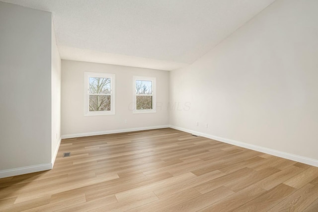 unfurnished room with light wood-type flooring, visible vents, and baseboards