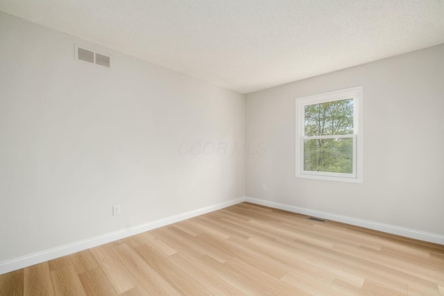 unfurnished room featuring light wood finished floors, baseboards, visible vents, and a textured ceiling