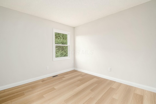 empty room featuring light wood-style floors, baseboards, and visible vents