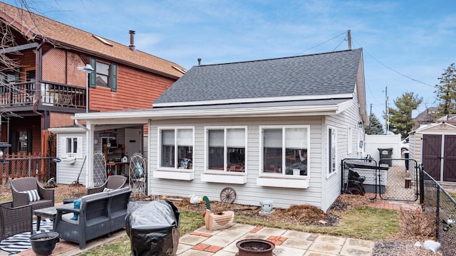 back of house with a fenced backyard, a fire pit, a storage shed, roof with shingles, and a patio area