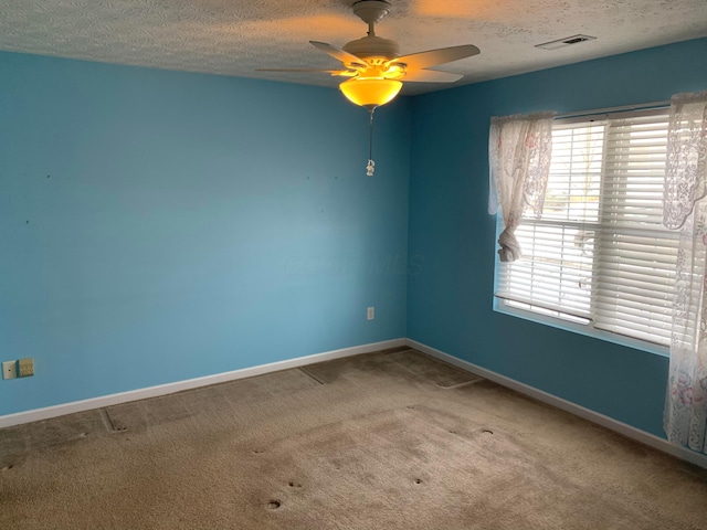 carpeted spare room with a ceiling fan, visible vents, a textured ceiling, and baseboards