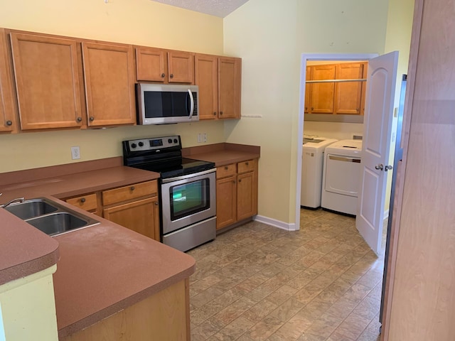 kitchen with baseboards, brown cabinets, stainless steel appliances, washing machine and dryer, and a sink