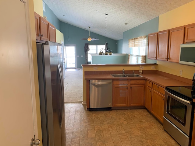 kitchen with stainless steel appliances, a peninsula, a sink, vaulted ceiling, and brown cabinets