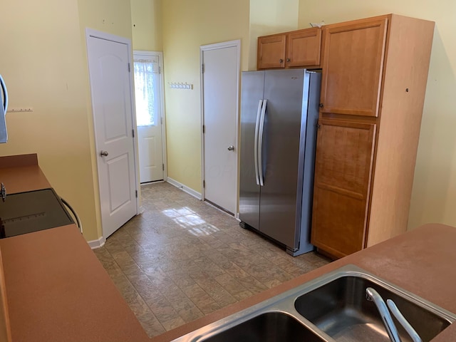 kitchen featuring light floors, light countertops, brown cabinetry, freestanding refrigerator, and baseboards