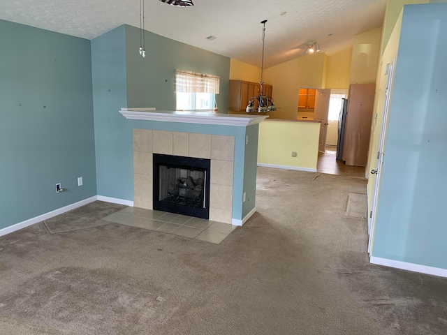 unfurnished living room with light carpet, vaulted ceiling, a textured ceiling, and a tiled fireplace