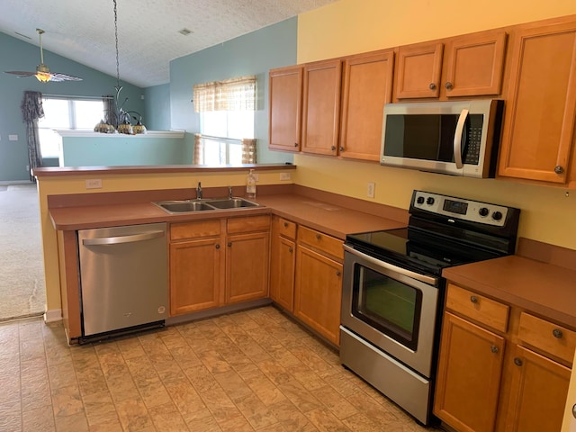 kitchen with appliances with stainless steel finishes, brown cabinets, a peninsula, a textured ceiling, and a sink