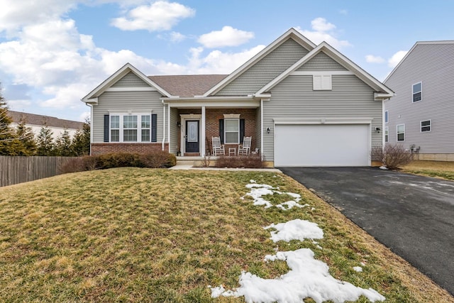 view of front of house with driveway, brick siding, covered porch, fence, and a front yard