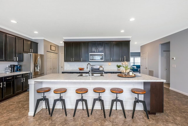 kitchen with a center island with sink, appliances with stainless steel finishes, ornamental molding, a kitchen bar, and a sink