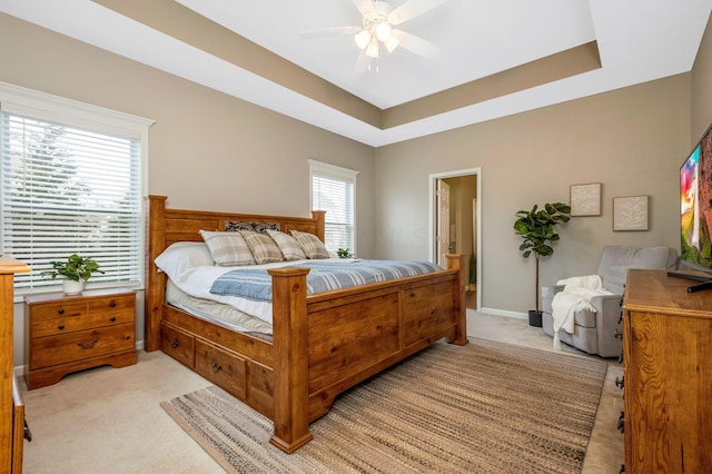 bedroom featuring a tray ceiling, light colored carpet, ceiling fan, and baseboards