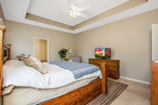 bedroom with a ceiling fan, a raised ceiling, light carpet, and baseboards