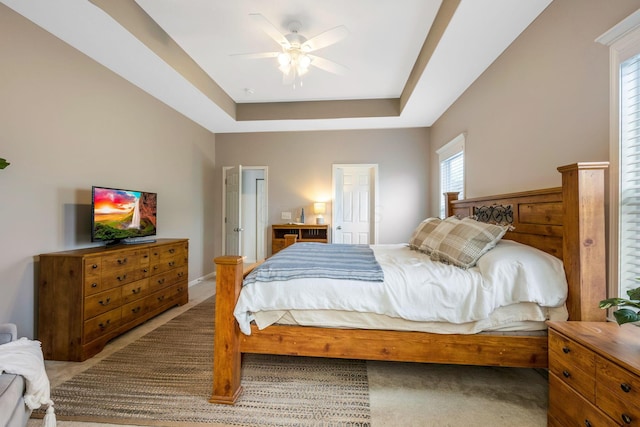 carpeted bedroom with ceiling fan and a tray ceiling