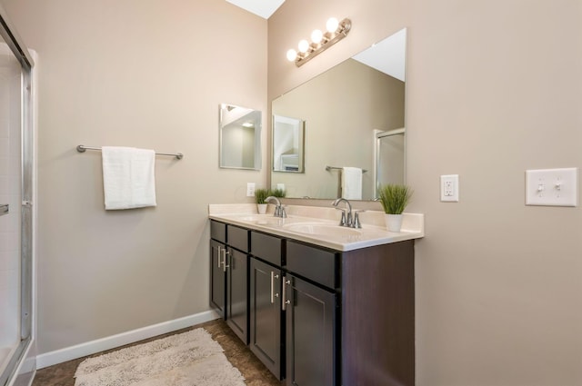 full bath with double vanity, an enclosed shower, baseboards, and a sink