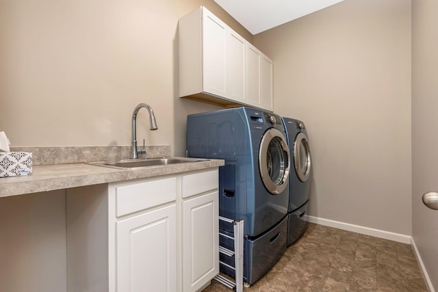 laundry area featuring washing machine and dryer, cabinet space, a sink, and baseboards