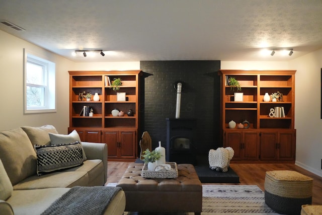 living area featuring a textured ceiling, a wood stove, visible vents, light wood finished floors, and rail lighting