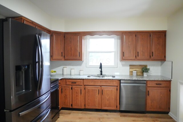 kitchen featuring appliances with stainless steel finishes, brown cabinets, light stone countertops, light wood-type flooring, and a sink