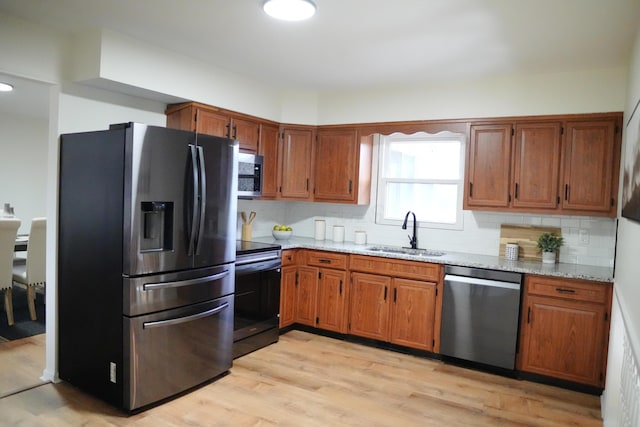 kitchen featuring light stone counters, brown cabinets, stainless steel appliances, decorative backsplash, and a sink