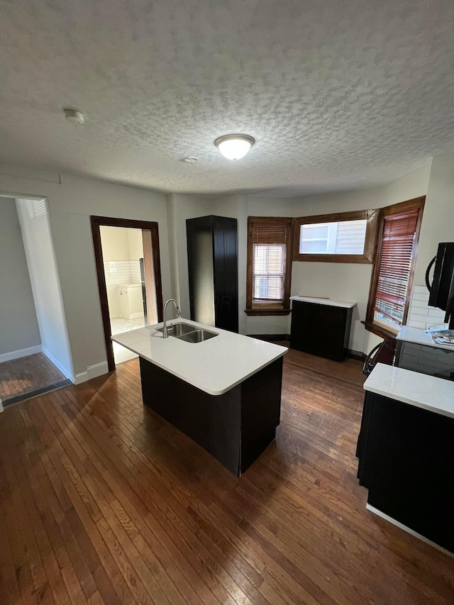 kitchen featuring dark wood-type flooring, light countertops, a sink, and a center island