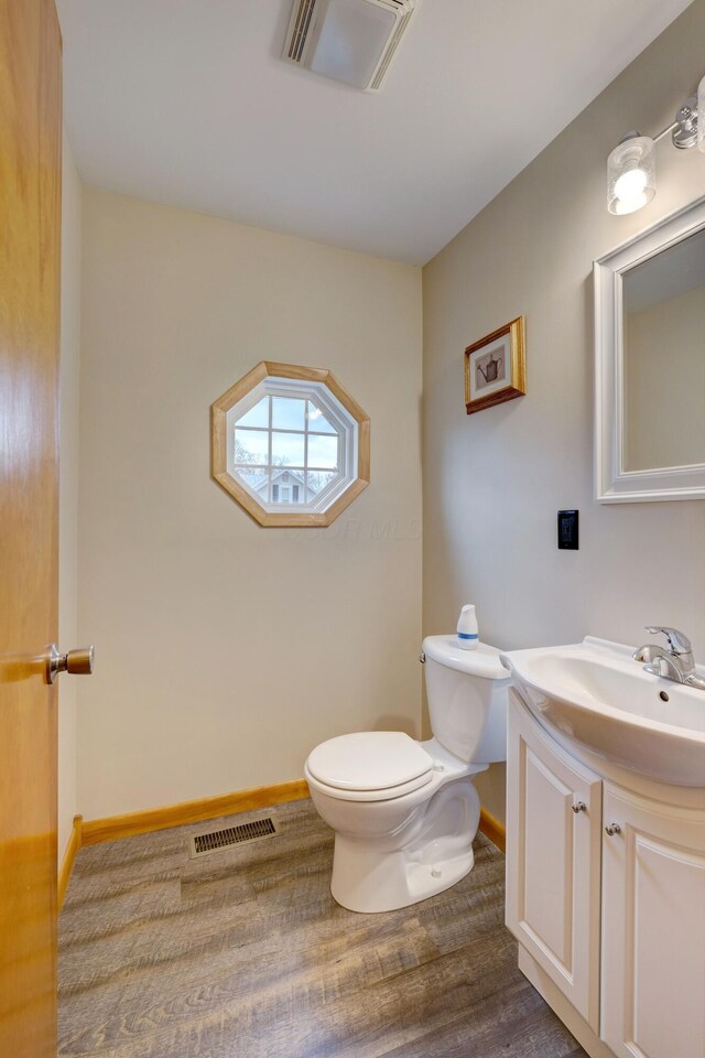 half bathroom featuring toilet, visible vents, wood finished floors, and vanity