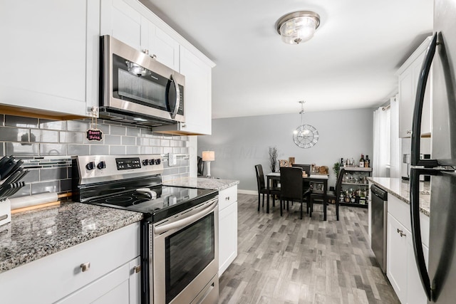 kitchen featuring light stone countertops, stainless steel appliances, white cabinets, decorative backsplash, and light wood finished floors