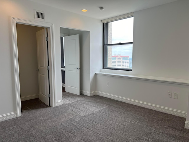 unfurnished bedroom with dark colored carpet, visible vents, and baseboards