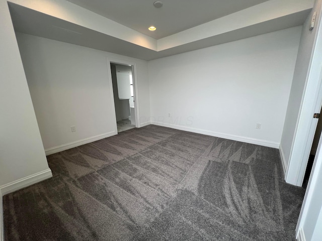 unfurnished bedroom featuring dark colored carpet, a tray ceiling, recessed lighting, and baseboards