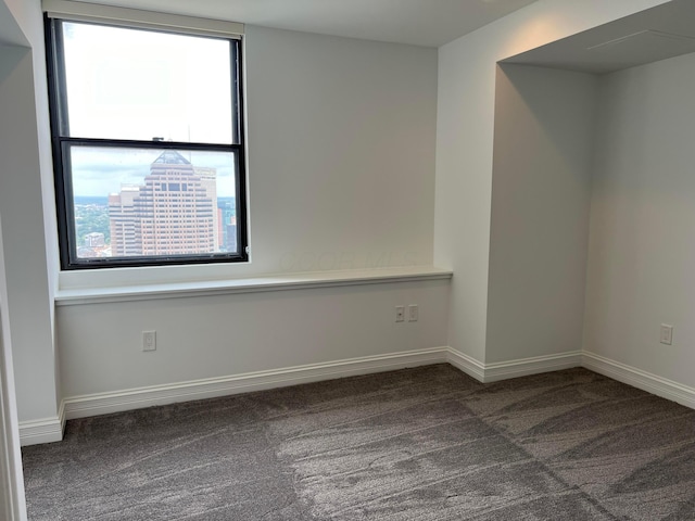 empty room featuring baseboards, dark carpet, and a city view